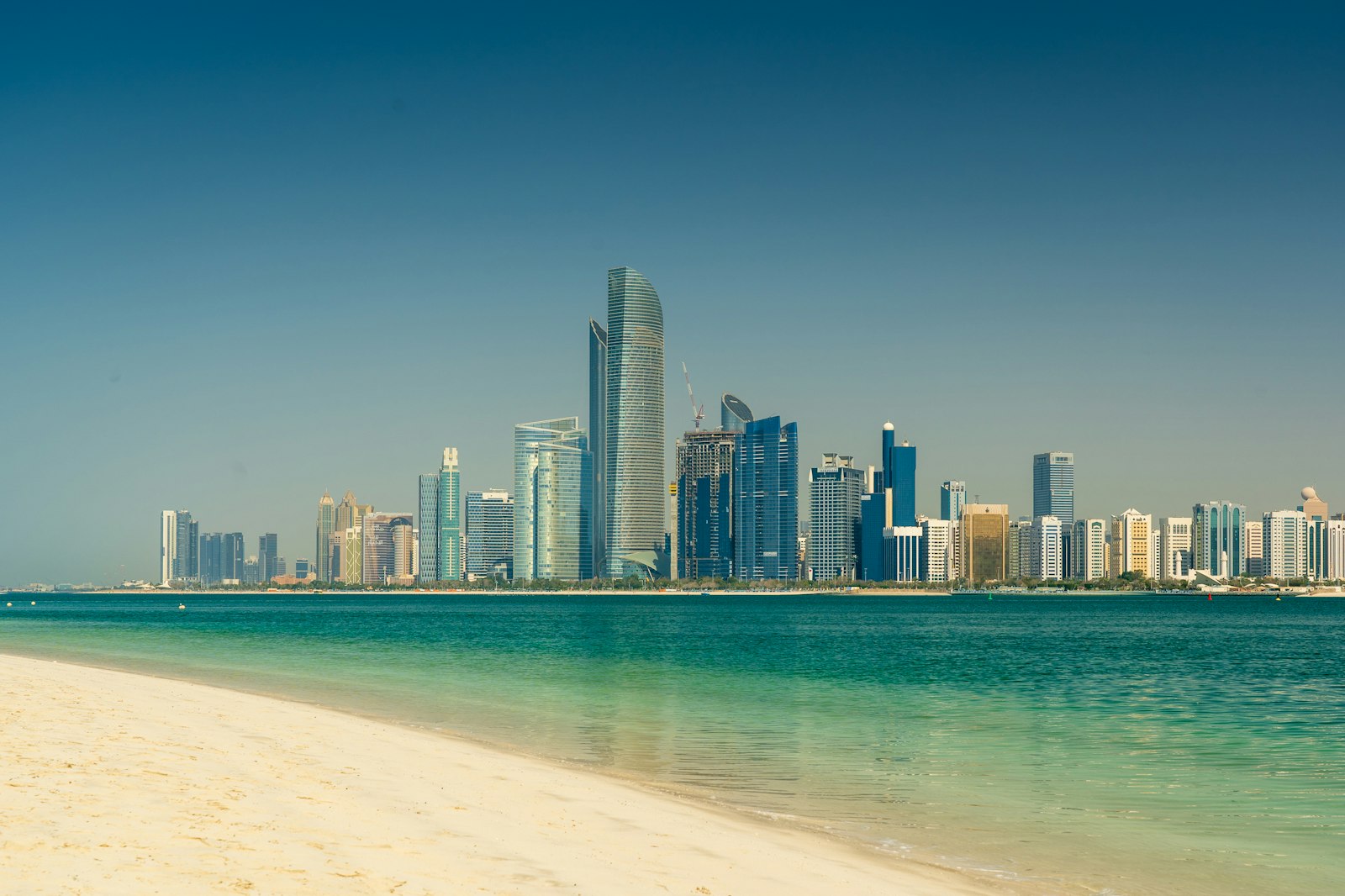 The Abu Dhabi skyline seen across the sea from a white sand beach